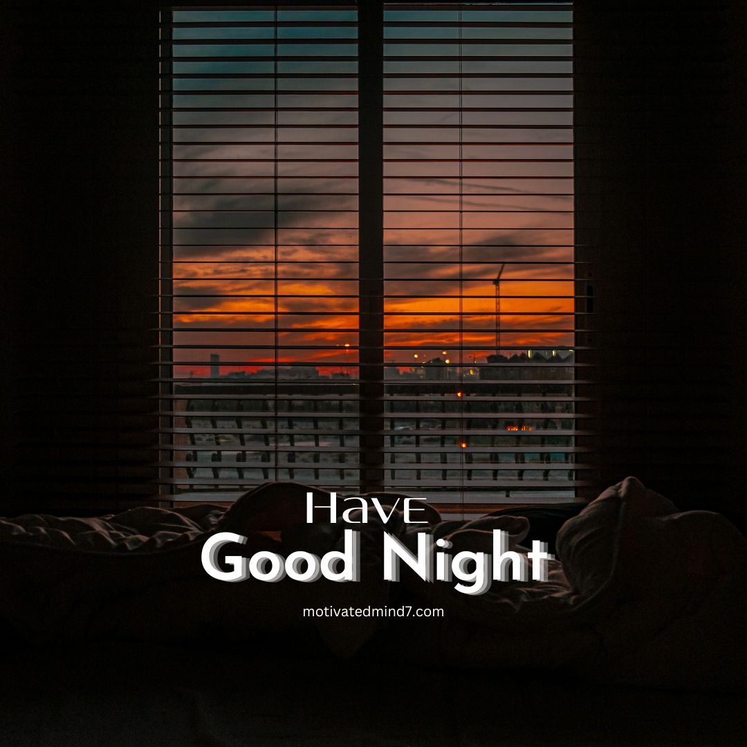 Inspirational Good Night Quote: 'Have Good Night' prominently displayed in the center of the image. The background features a serene view through a window with horizontal blinds partially open, revealing a sunset or sunrise with vibrant orange and red hues in the sky. The silhouette of a cityscape with buildings and possibly a wind turbine or tower is visible in the background. In the foreground, there is a bed with rumpled sheets and pillows, creating a cozy and tranquil atmosphere.